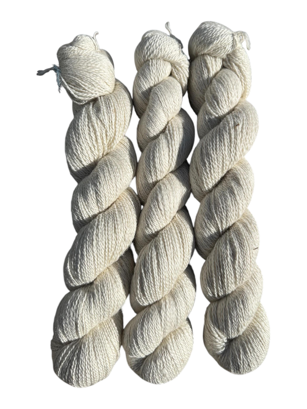 Three skeins of Oak Crest Alpacas and More natural undyed fingering weight alpaca yarn in a soft cream color.