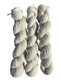 Three skeins of Oak Crest Alpacas and More natural undyed fingering weight alpaca yarn in a soft cream color.